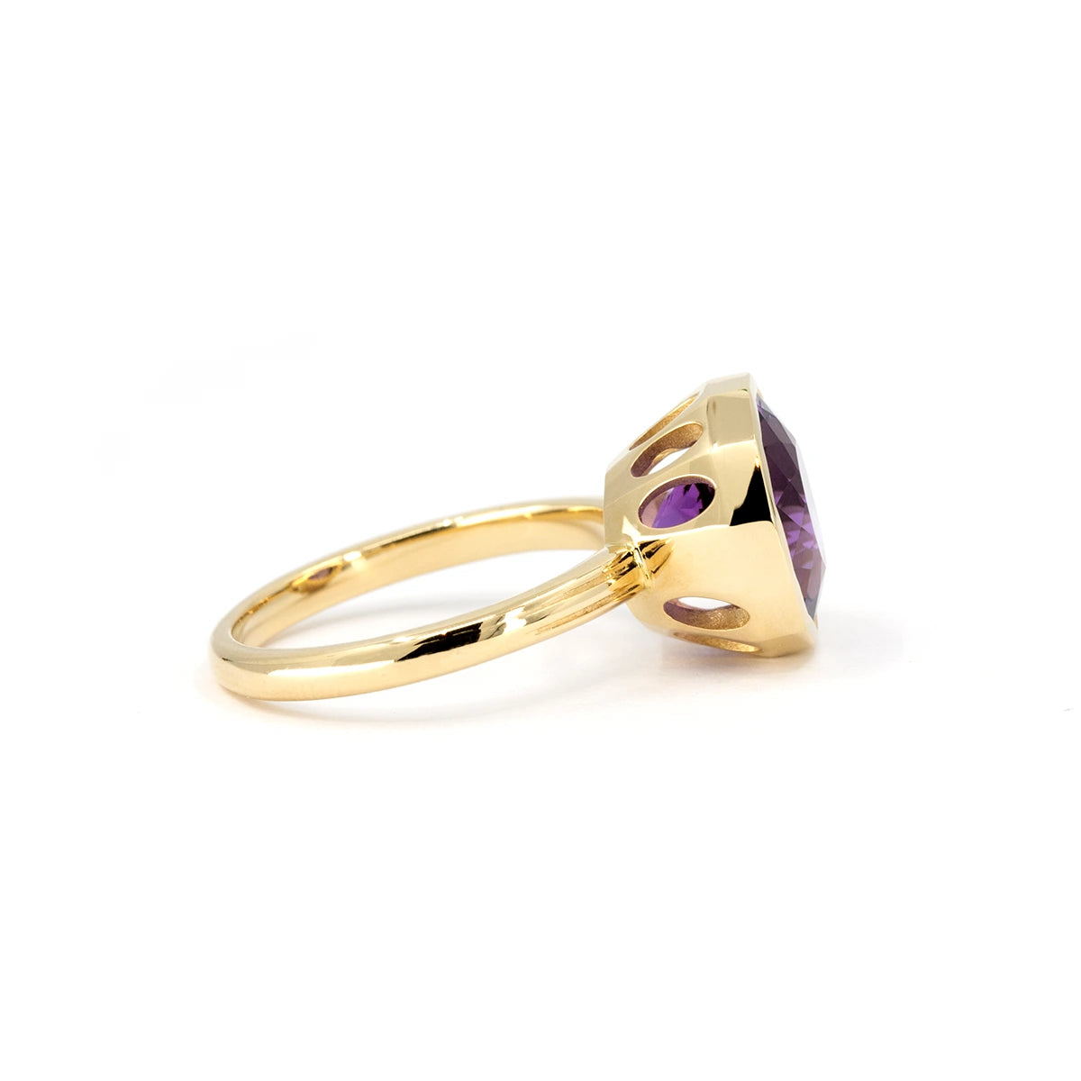 Side view of a yellow gold amethyst ring by Bena Jewelry, featuring an elegant design with oval cutouts in the band. The openings allow light to beautifully illuminate the gemstone, enhancing its stunning purple color and unique style.