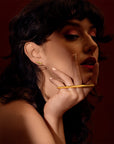 Darkly mysterious fashion photography of a fabulous gold ring that is the full width of a fist, worn on two fingers with a double band. The jewel is worn by a brunette with a cool attitude. The jewel is unisex and was designed by independent designer Bena Jewelry.