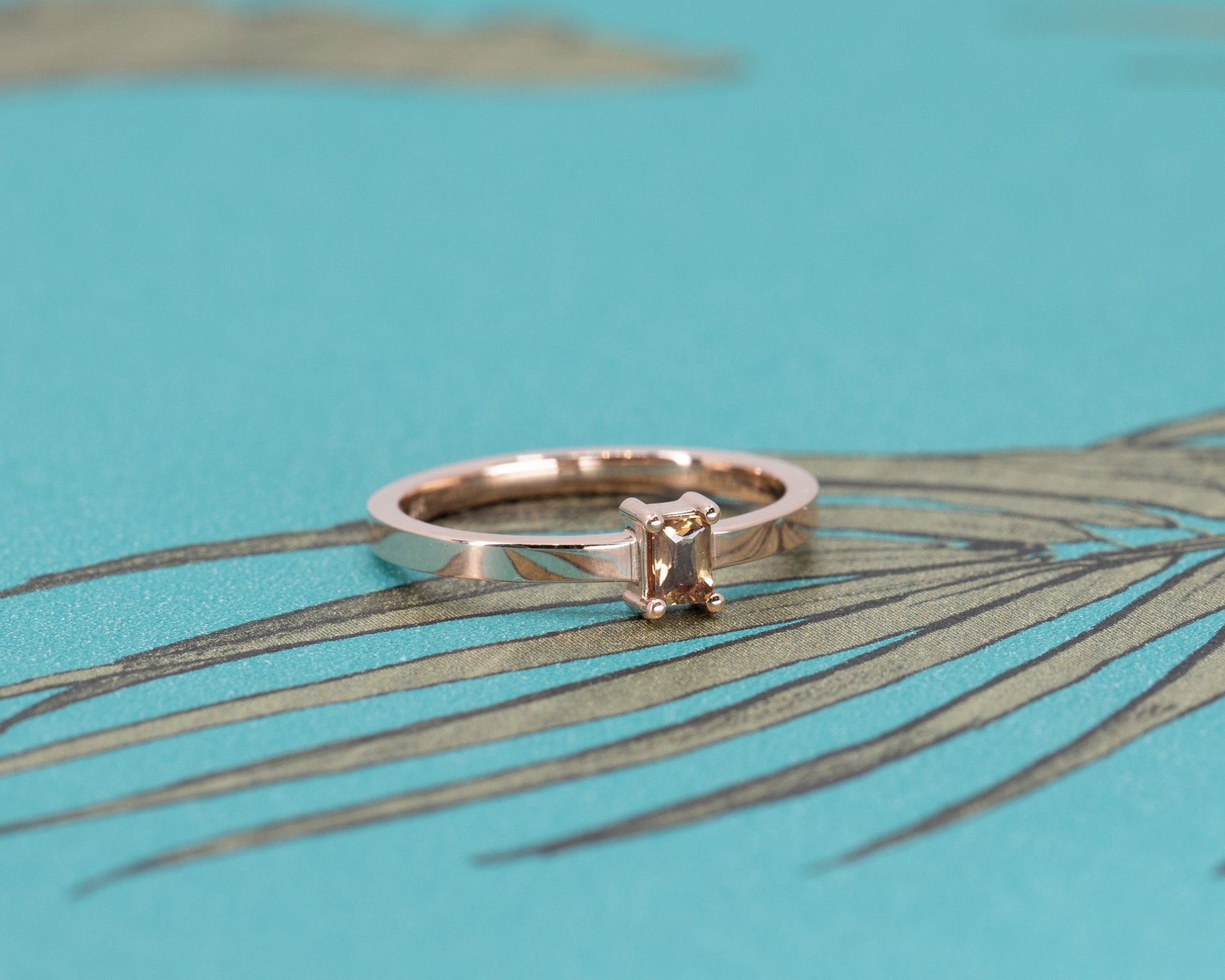 Close-up of Bena Jewelry's rose gold ring with an orange sapphire and diamond accents, set against a white background.