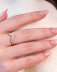 Close-up of a yellow gold V-shape wedding band with round and pear-shaped diamonds, worn on a finger with light pink nails and a white/beige sweater.