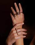 Studio high end jewelry fashion shoot. Dark background almost black. All that lights up are two women's hands wearing luxurious yellow gold and diamond jewelry, all created by independent Canadian brand Bena Jewelry.