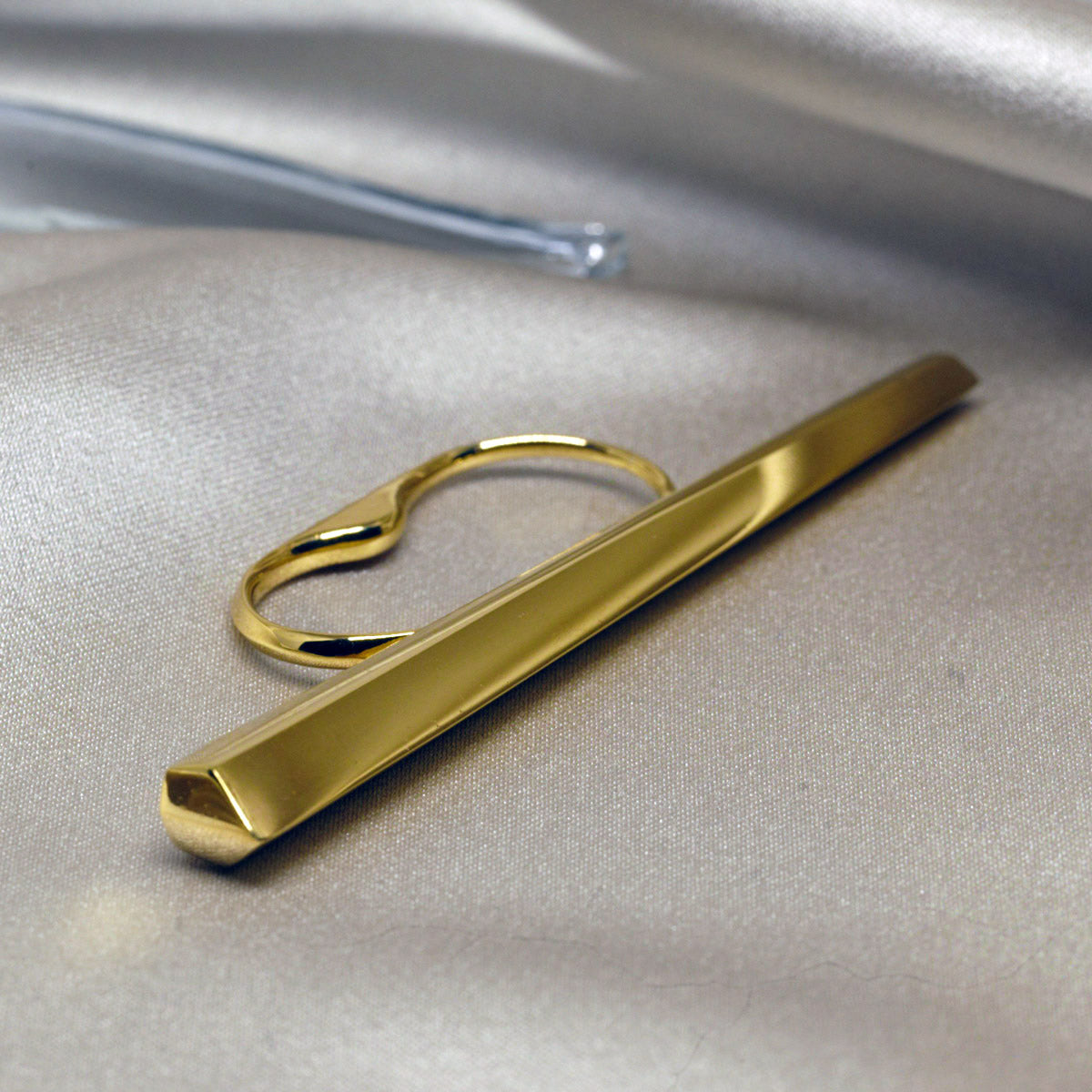 Close-up of a solid gold ring with a lot of character, consisting of a long block of gold with studied shapes that spans the entire width of the fist and is worn on two fingers with a comfortable double band. It's by Montreal-based designer Bena Jewelry, who creates modern, elegant, gender-neutral jewelry that reflects light in a unique way.