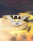 Front view of a yellow gold diamond wedding band by Bena Jewelry, featuring round and pear-shaped diamonds. Set against a warm, artistic abstract background in brown and yellow tones.