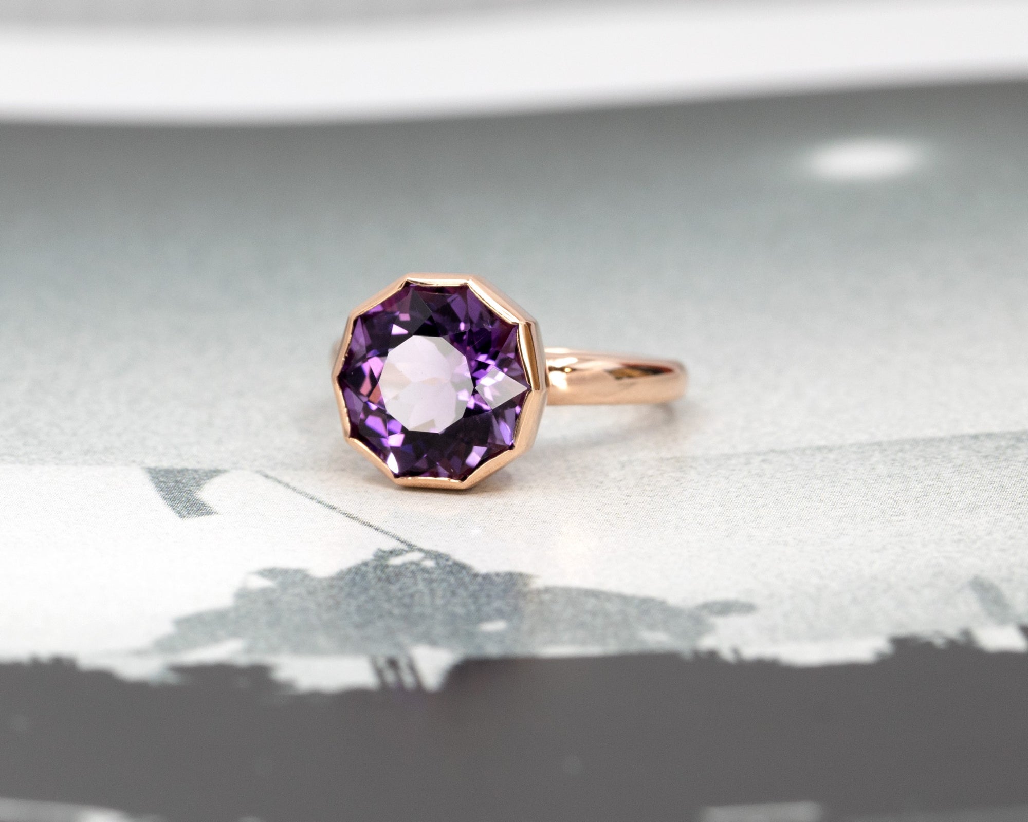 Round amethyst ring in yellow gold, glowing against a dark colored backdrop, designed by Bena Jewelry.