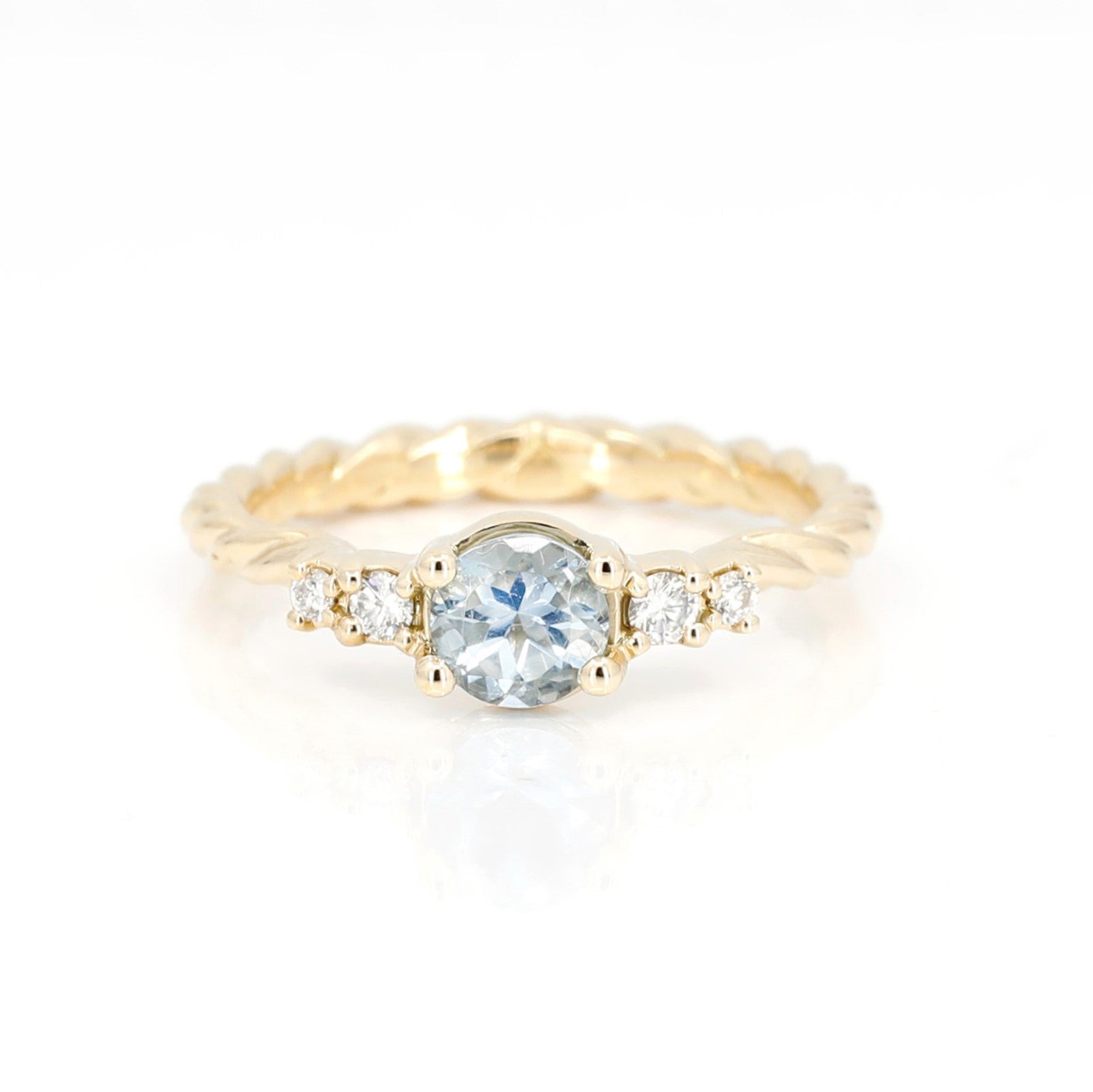 Top view: Showcasing the round aquamarine centerpiece and the diamonds on the braided yellow gold band. Made by Bena Jewelry in Montreal, Canada.