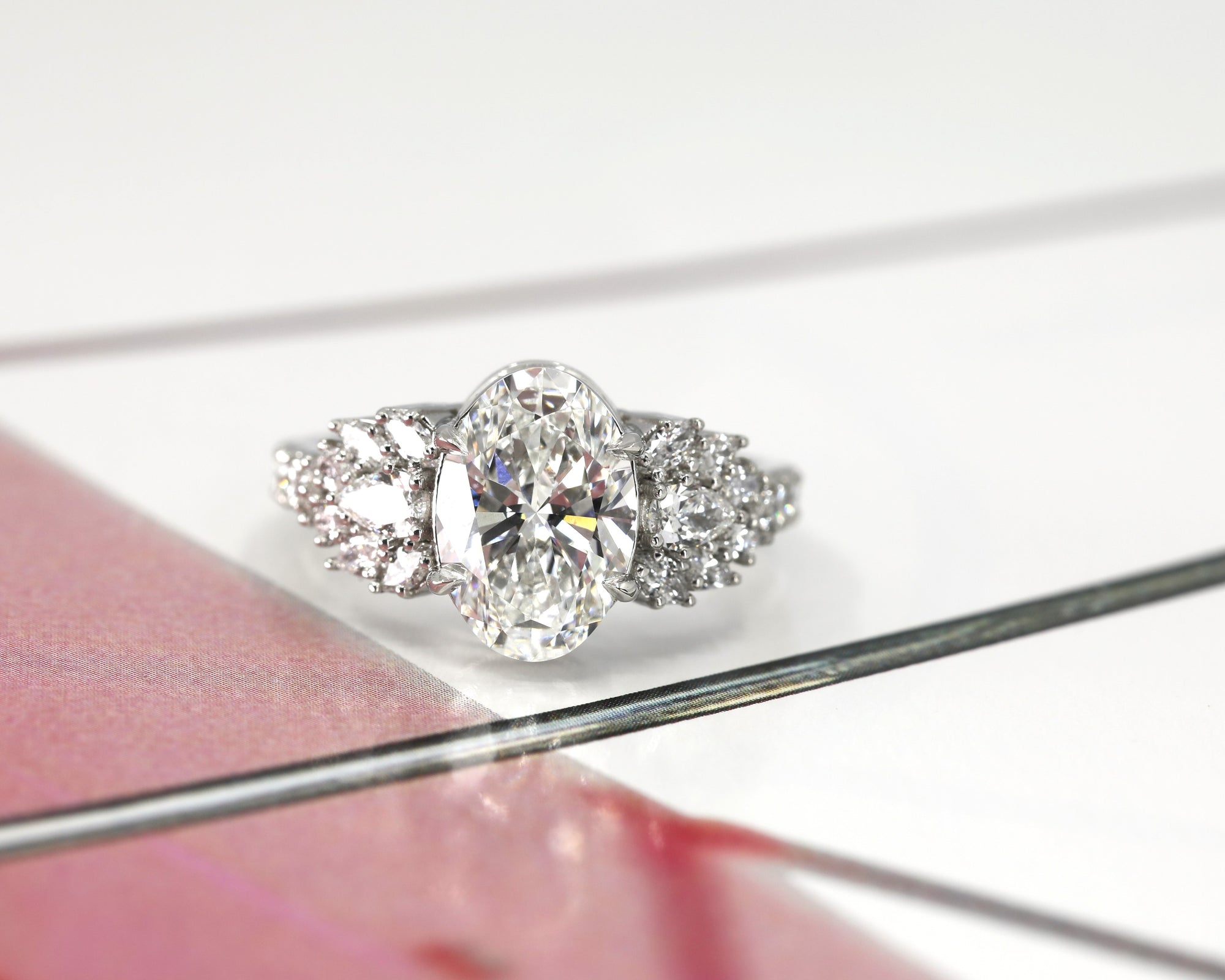 front view oval shape lab grown diamond and side gemstone designed by bena jewelry best bridal engagement ring desginer in montreal bespoke engagement ring in platinum and lab grown diamonds on multi color background