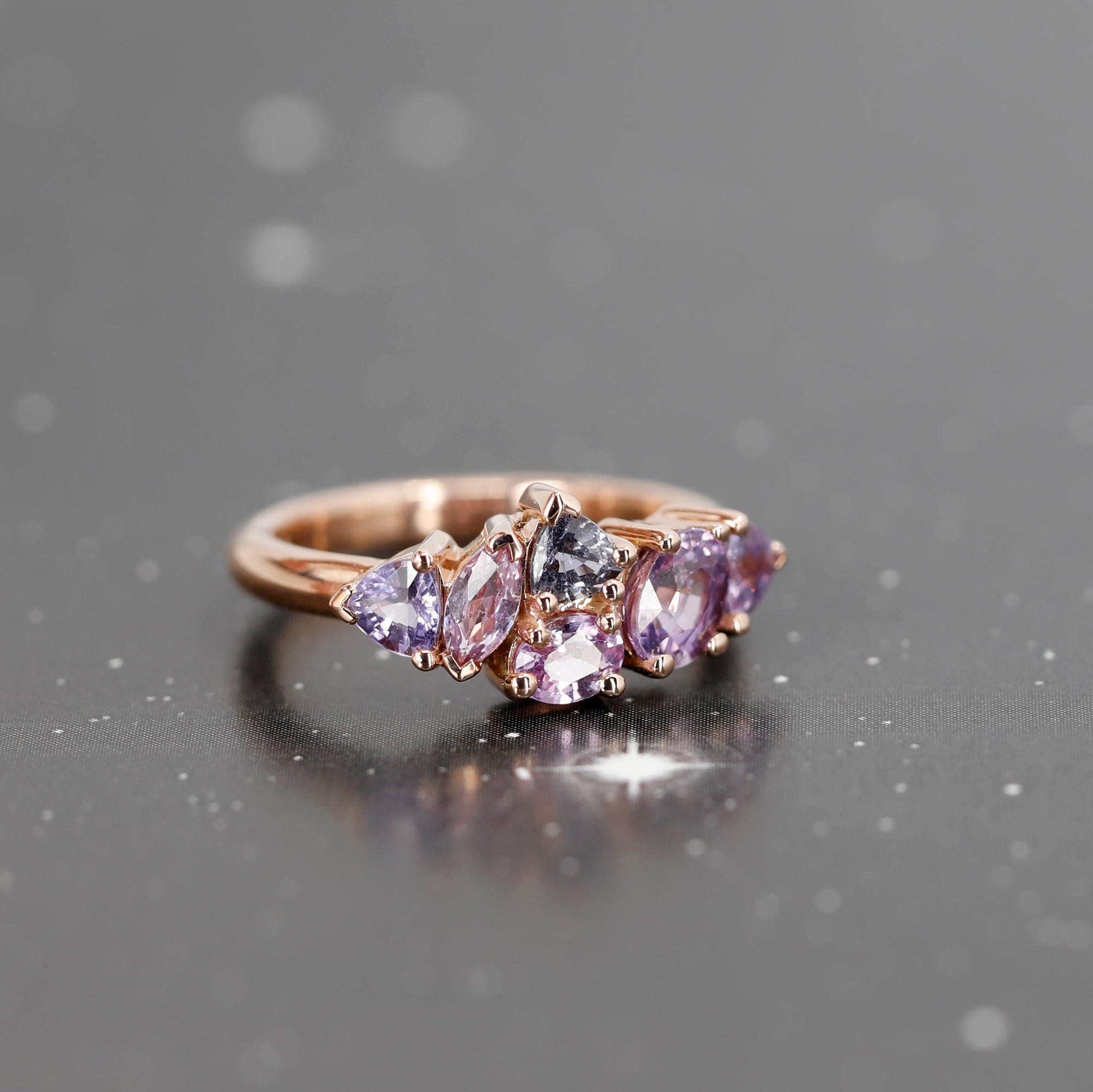 The "Avalanche" ring, set with lilac and purple sapphires in rose gold, showcased on a shadowy backdrop for a dramatic and elegant contrast. A modern masterpiece crafted in Montreal by Bena Jewelry.