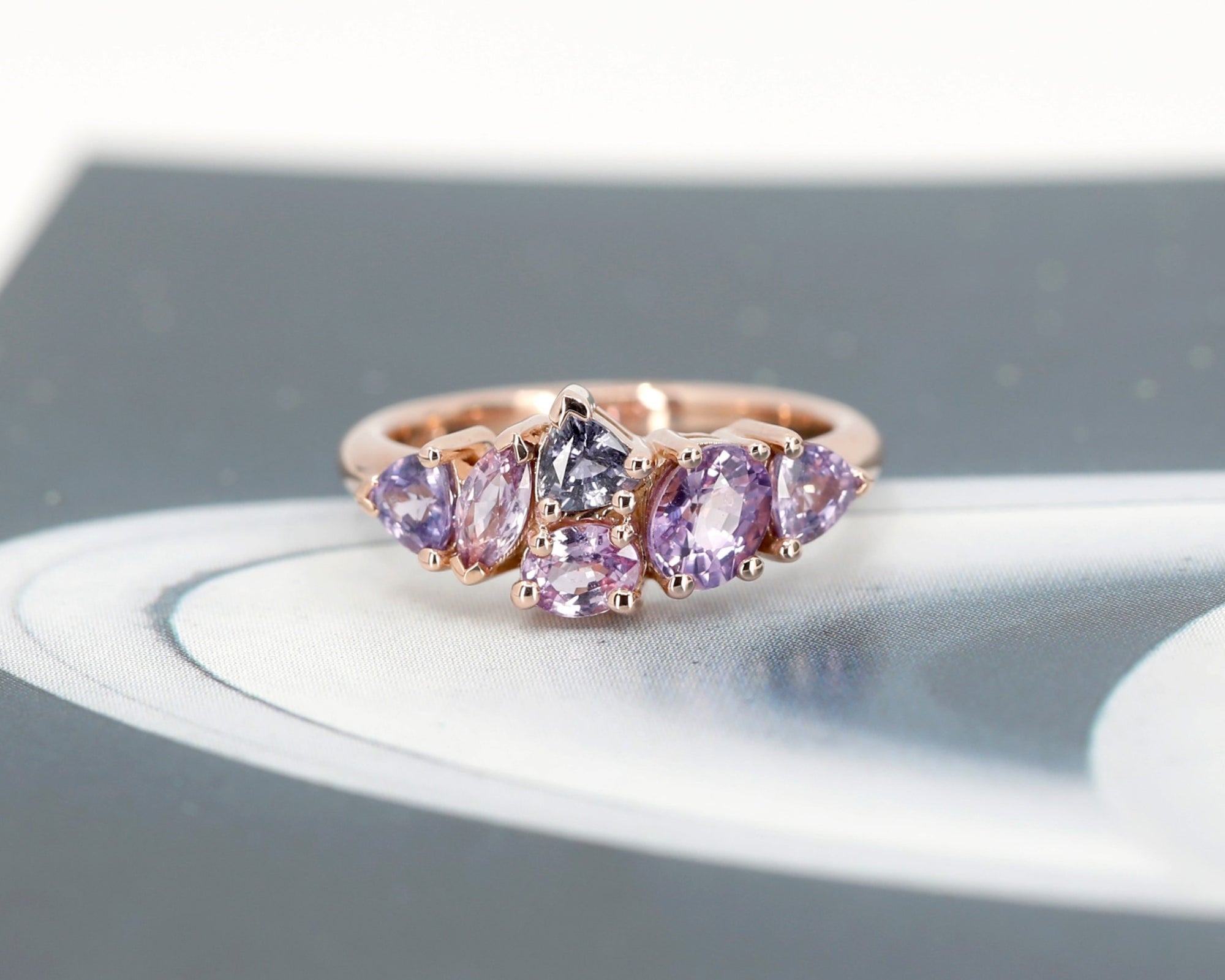 A striking view of the "Avalanche" ring in rose gold, featuring a cluster of lilac and purple sapphires. The dark background accentuates the vivid colors and contemporary design. Made in Montreal by Bena Jewelry.