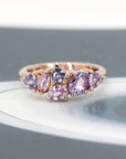 A striking view of the "Avalanche" ring in rose gold, featuring a cluster of lilac and purple sapphires. The dark background accentuates the vivid colors and contemporary design. Made in Montreal by Bena Jewelry.