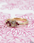 Artistic shot of Ruby & Salt And Pepper Diamond Avalanche Ring on soft rose-colored background, emphasizing the beautiful rubies and salt and pepper diamonds in yellow gold.