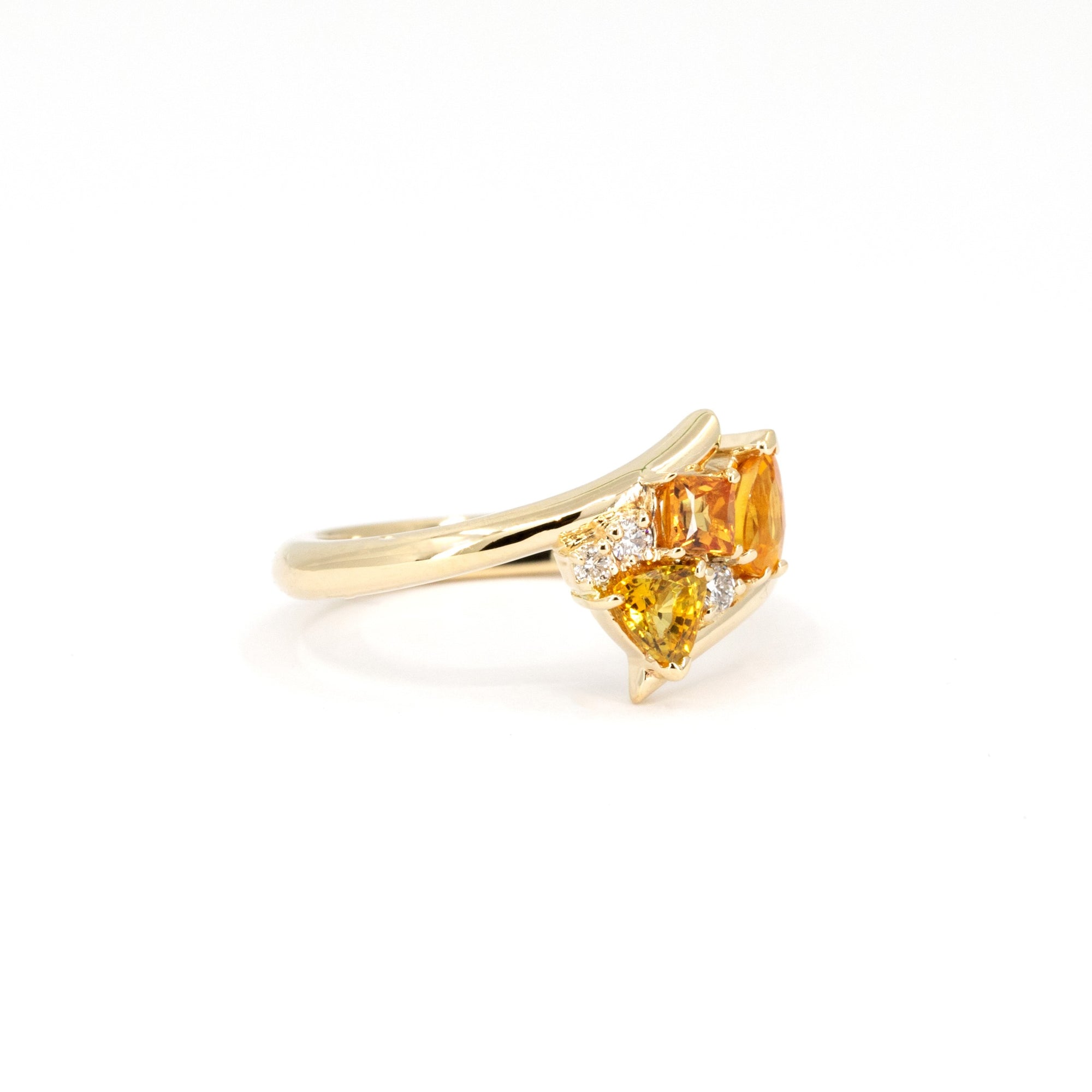Close-up of the Kink Avalanche ring showcasing the twist design and vibrant orange and yellow sapphires, set in yellow gold.