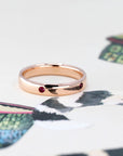 Elegant men’s rose gold wedding band with pigeon blood rubies, displayed on a soft-toned background. Designed by Bena Jewelry in Montreal.