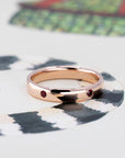 Rose gold ring with bezel-set rubies, styled on a light background. Handmade by Bena Jewelry, a Canadian jewelry designer.