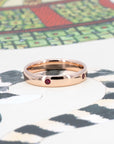 Subtle dome wedding band in rose gold with vivid pigeon blood rubies, photographed on a pastel backdrop by Bena Jewelry.