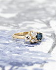 Custom blue spinel and diamond ring in yellow gold, showcased against a light blue background, designed by Bena Jewelry.