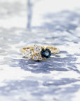 Yellow gold ring with blue spinel and diamonds, displayed on a soft blue background, crafted by Bena Jewelry in Montreal.