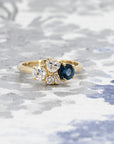 Bespoke fine jewelry featuring a blue spinel and diamonds in yellow gold, styled on a pale blue background.