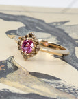 Lifestyle image of yellow gold ring with pink sapphire and brown diamonds by Bena Jewelry, photographed in Montreal with a colorful styled setting.