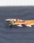 A striking view of the "Kink Demantoid" ring on a shadowy backdrop, emphasizing the vivid green garnet and the sleek rose gold design. The dark tones create an elegant and powerful presentation of this edgy, contemporary piece by Bena Jewelry, made in Montreal.