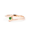A close-up of the "Kink Demantoid" ring in rose gold, showcasing a vivid green demantoid garnet in a bezel setting. The minimalist design and sleek lines stand out against the white background, emphasizing the gemstone’s brilliance. Crafted in Montreal by Bena Jewelry, edgy contemporary fine jewelry.