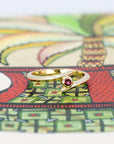 Front view of Edgy Kink Ruby ring in yellow gold with a bezel-set blood-red ruby, presented against a bold colored backdrop. A contemporary piece by Bena Jewelry, crafted in Montreal.
