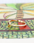 Sid view of Kink Ruby ring with a round blood-red ruby in a bezel setting on a yellow gold twisted band, displayed on a vibrant colored background. Designed by Bena Jewelry in Montreal.