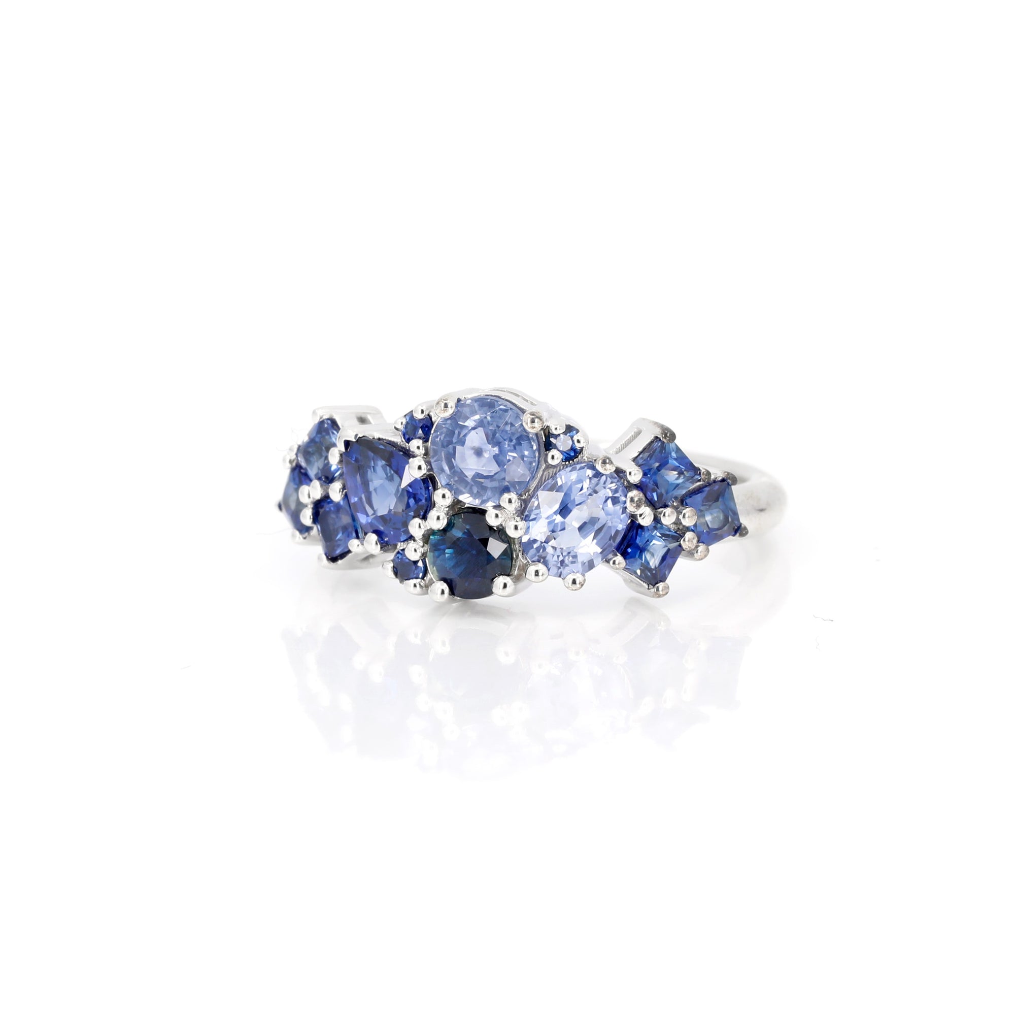 Angled side view: Highlights the interplay of royal blue and cornflower sapphires with the refined white gold band. Crafted by Bena Jewelry, Montreal, Canada.