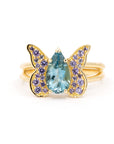 Butterfly-inspired ring in yellow gold featuring a pear-cut aquamarine center stone and a pavé of purple sapphires. Designed and handcrafted in Montreal by Bena Jewelry.