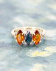 front view of bena jewelry custom made trilogy colored gemstone citrine and sapphire marquise shape as well as brown diamond on multi color background
