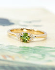 Cushion-cut green sapphire engagement ring with side diamonds displayed on a light-colored background. Fine bridal jewelry designed by Bena Jewelry, made in Montreal.
