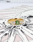 Green sapphire cushion gemstone ring with lab-created pear diamond accents in a yellow gold setting. Designed by Bena Jewelry in Montreal, Canada.