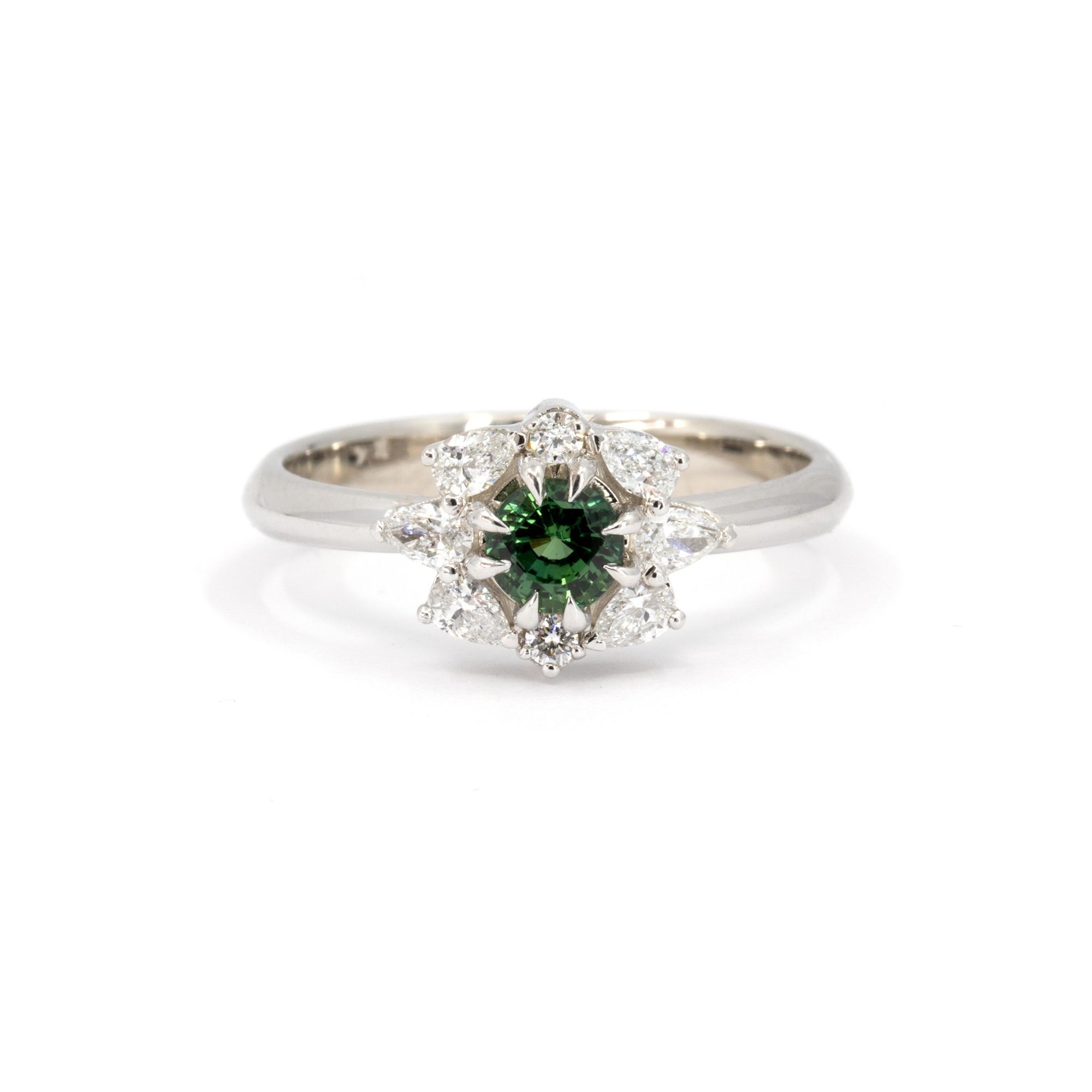 Close-up of the Deep Forest Glow ring in white gold, featuring a vibrant green sapphire at its center, surrounded by a diamond halo in a floral-inspired design. Handmade by Bena Jewelry in Montreal.