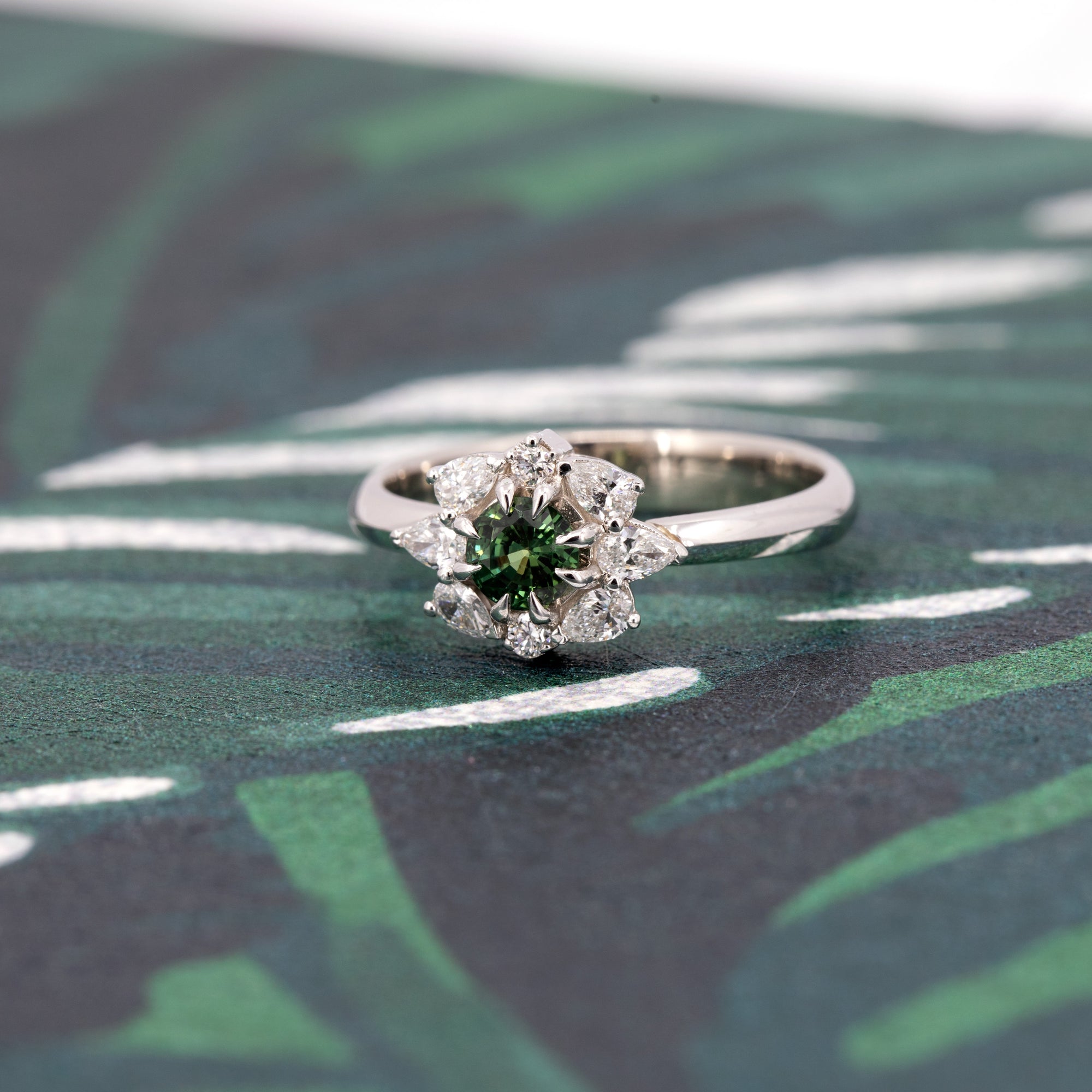 Dramatic lighting highlights the Deep Forest Glow ring, emphasizing the deep hues of the green sapphire and the brilliance of the diamond accents against a moody backdrop.