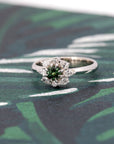 Dramatic lighting highlights the Deep Forest Glow ring, emphasizing the deep hues of the green sapphire and the brilliance of the diamond accents against a moody backdrop.
