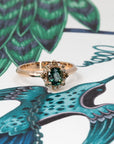 Teal sapphire and diamond halo ring in rose gold by Bena Jewelry, photographed on a soft pink-beige background in Montreal.