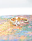 Elegant yellow gold engagement ring featuring a round diamond and side accents Round Diamond Desir Ring by Bena Jewelry photographed on a vibrant colored backdrop