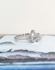 Elegant white gold engagement ring featuring a central pear-shaped diamond and side stones, styled on a warm-toned backdrop. Made by Bena Jewelry.