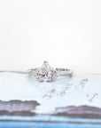 Custom white gold ring with a pear-shaped diamond and side accents, photographed on a colorful background. Designed by Bena Jewelry in Montreal, Canada.