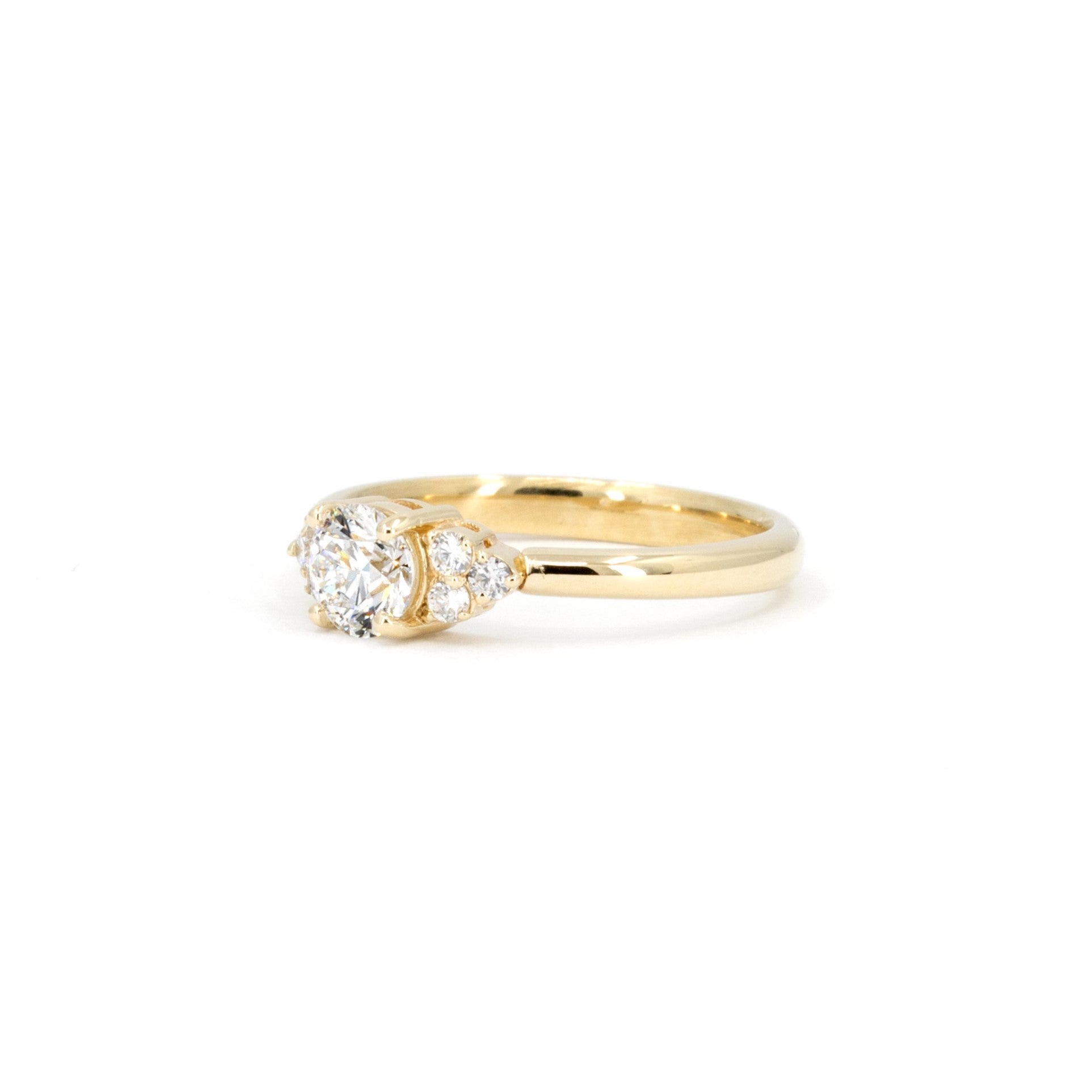 Montreal-made yellow gold engagement ring with a round diamond and sparkling side stones, styled on a white background by Bena Jewelry.