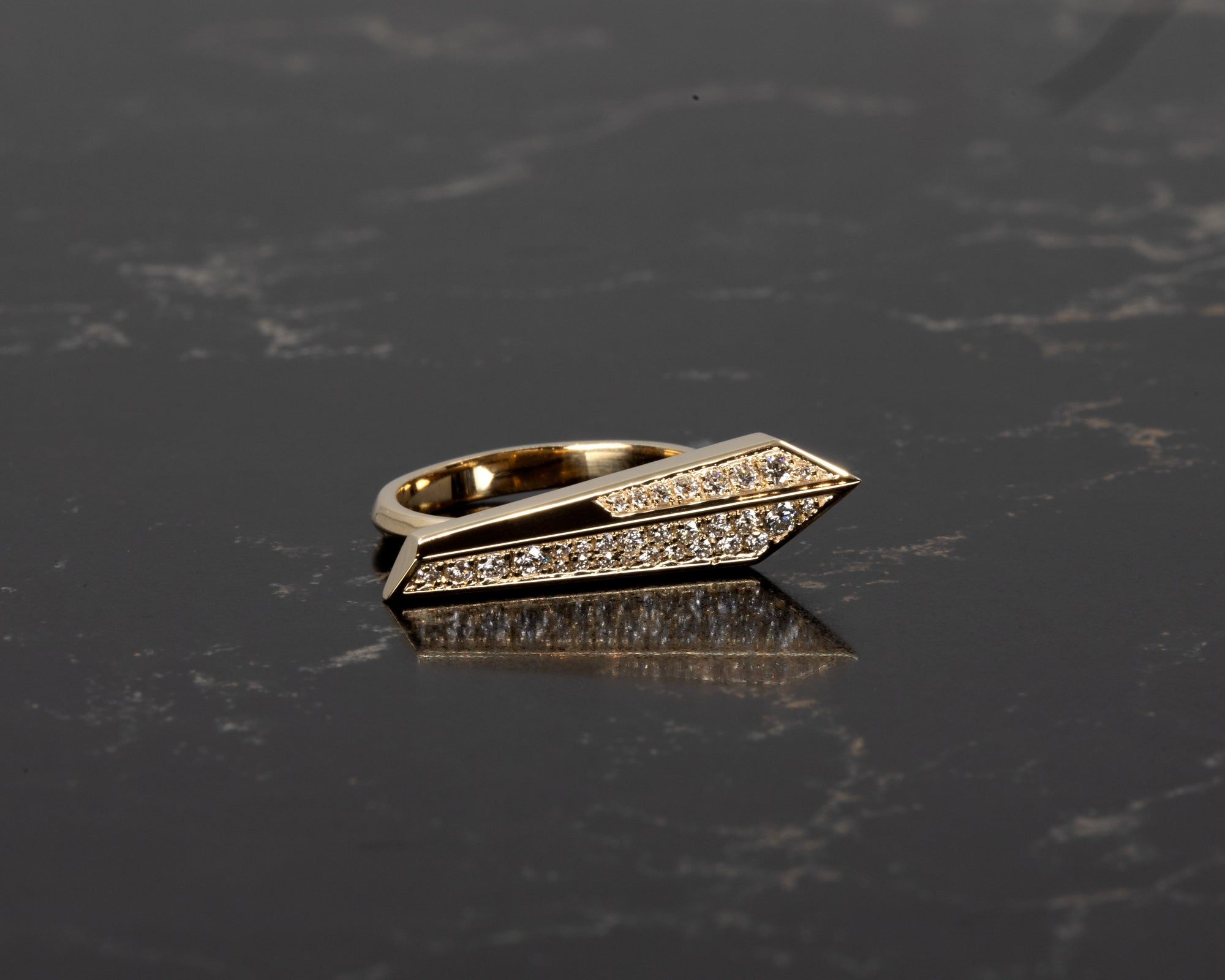 Architectural diamond ring in rich yellow gold by Bena Jewelry, glowing under soft shadows on a dark background, showcasing modern design details.