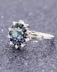 Soleil Ring displayed on glittering background, featuring blue diamond, sapphire halo, and bold white gold band.