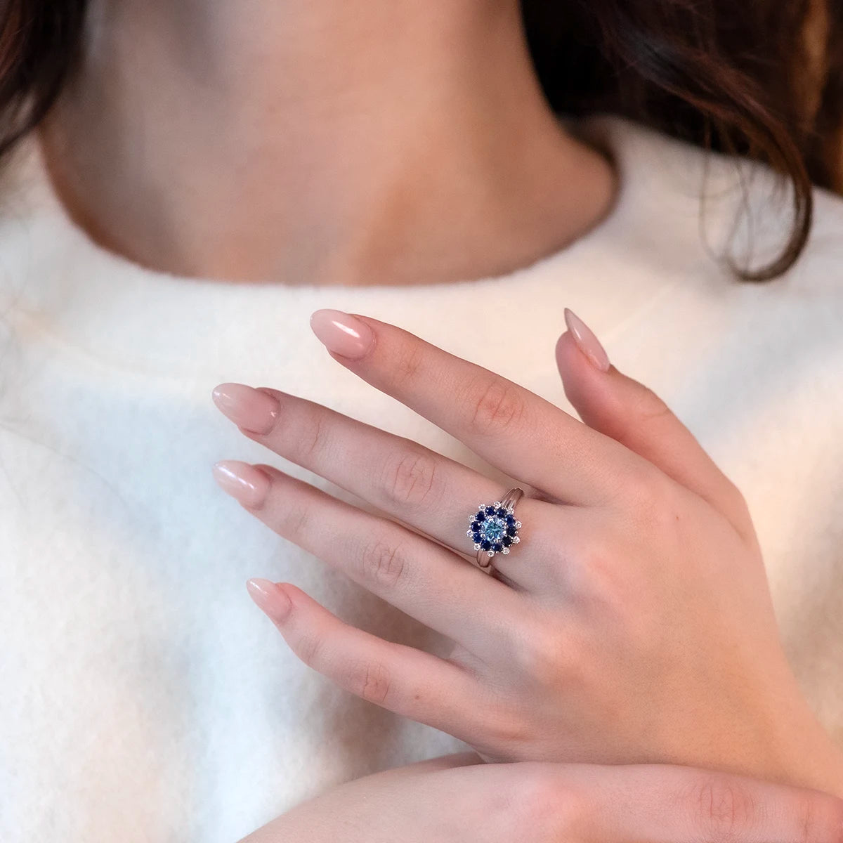 Model wearing the Soleil Ring by Bena Jewelry, bold white gold ring with blue diamond centerpiece and sapphire halo.