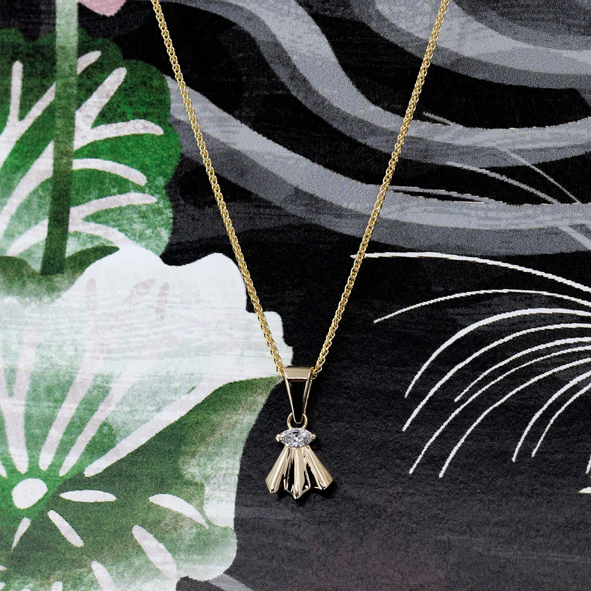 Yellow gold pendant with a marquise diamond, displayed against an artistic floral and abstract black background. The unique fan-shaped design by independent Montreal-based brand Bena Jewelry highlights timeless elegance and craftsmanship.