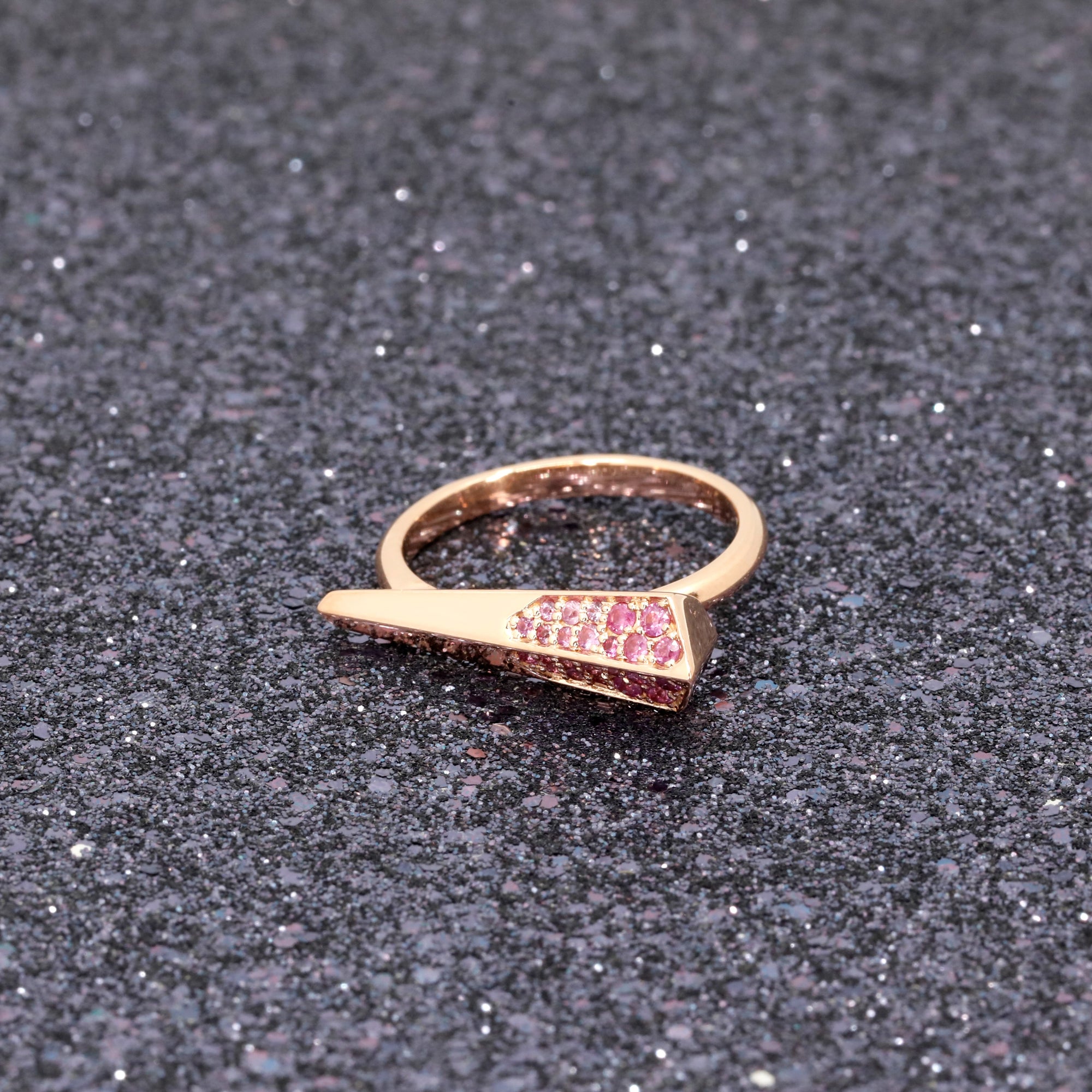 Pink Sapphire Spine Ring with vibrant pink sapphires in rose gold, showcased on a dark glitter background, designed by Bena Jewelry.
