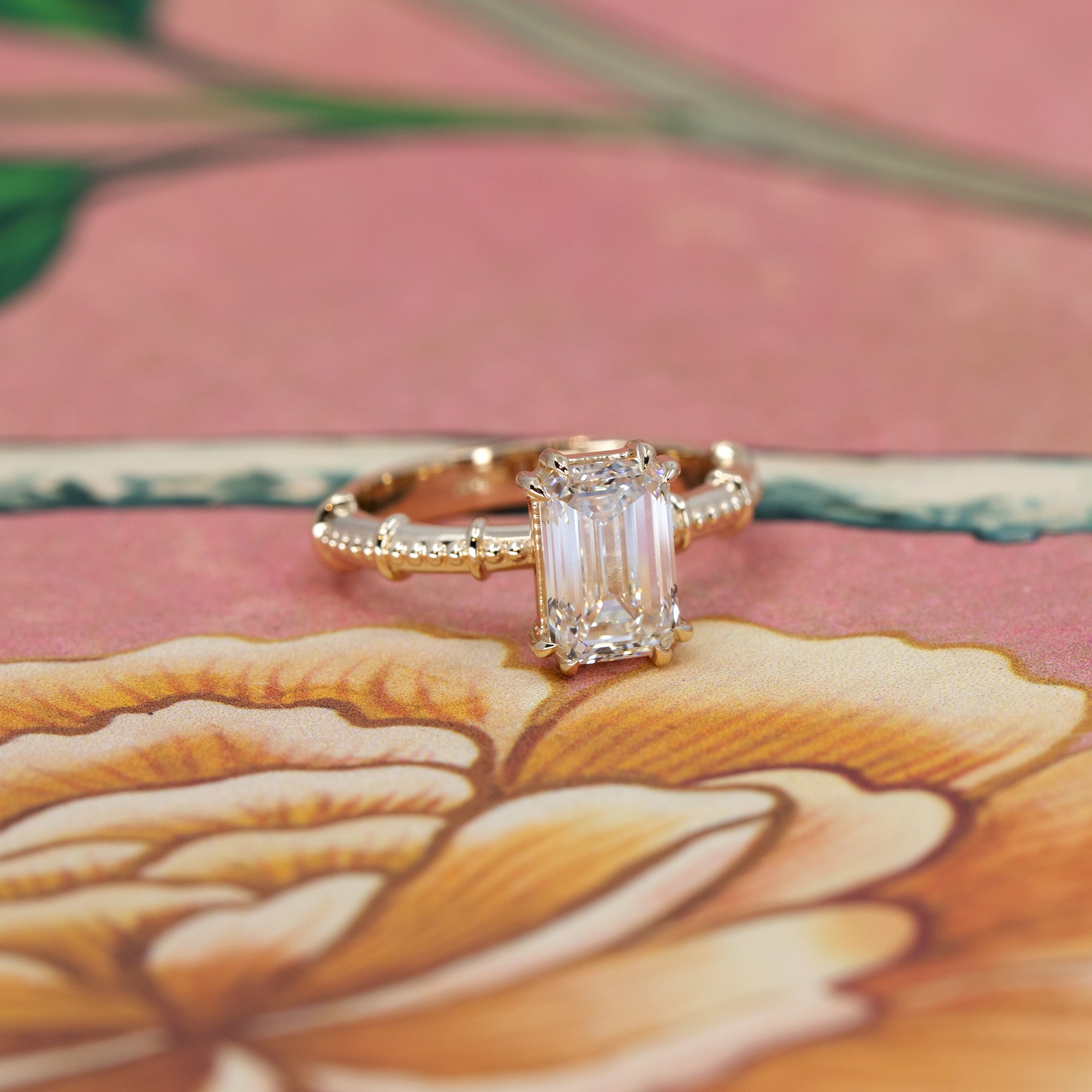 Close-up of the vintage-inspired engagement ring with an emerald-cut diamond and a finely detailed gold band.
