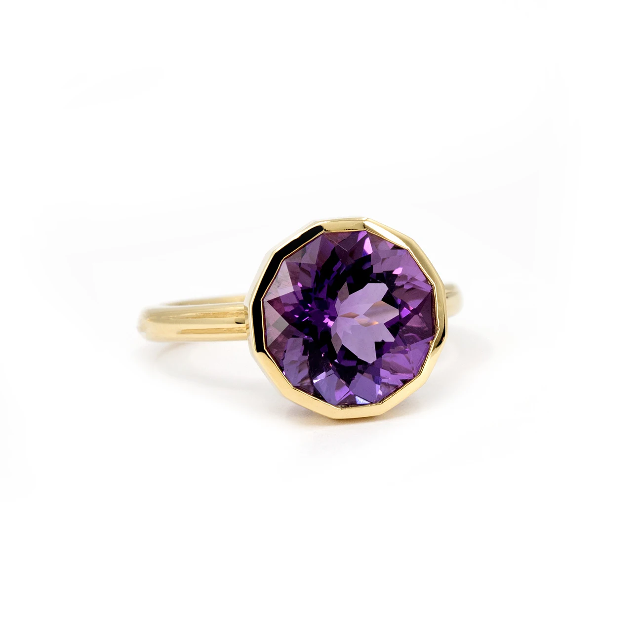 Close-up of a yellow gold amethyst ring by Bena Jewelry, highlighting the gemstone's vibrant purple hues and reflections within. The elegant design is showcased on a white background, emphasizing the light play inside the stone.
