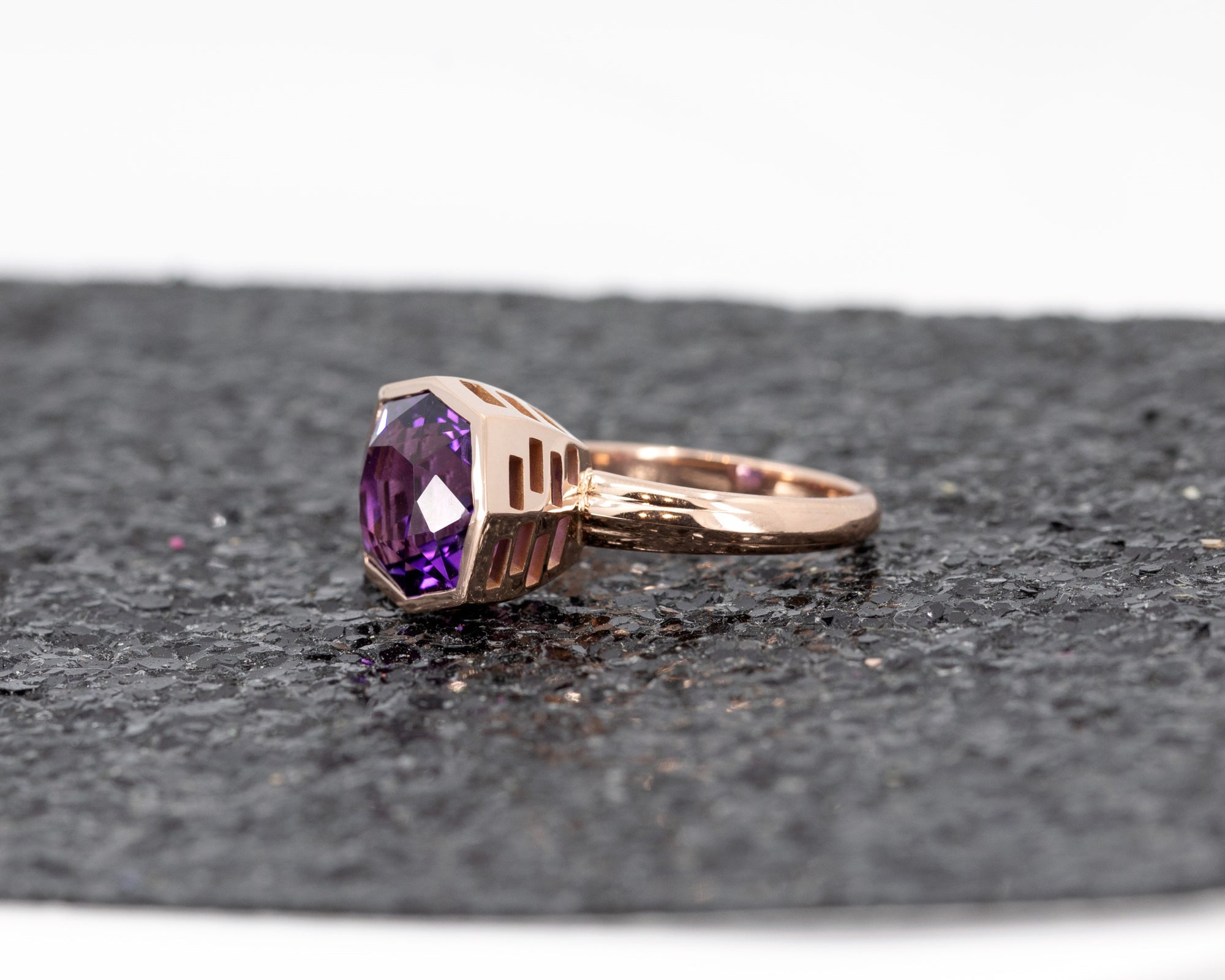 Bold statement amethyst ring by Bena Jewelry, with a robust rose gold band, photographed on a luxurious black glitter backdrop.