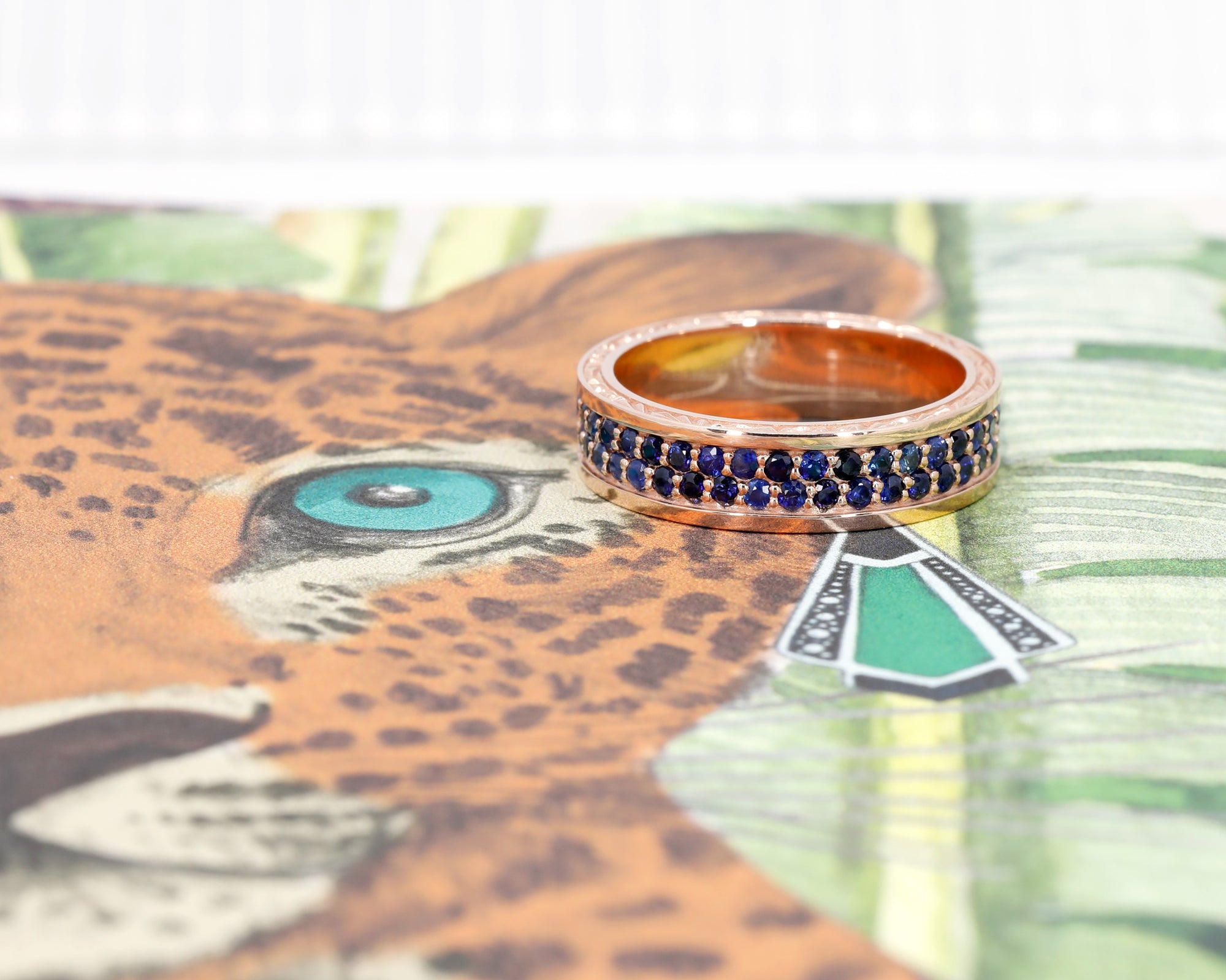 Rose Gold Sapphire Chiseled Ring with royal blue sapphires, displayed on a colored background, designed by Bena Jewelry in Montreal.