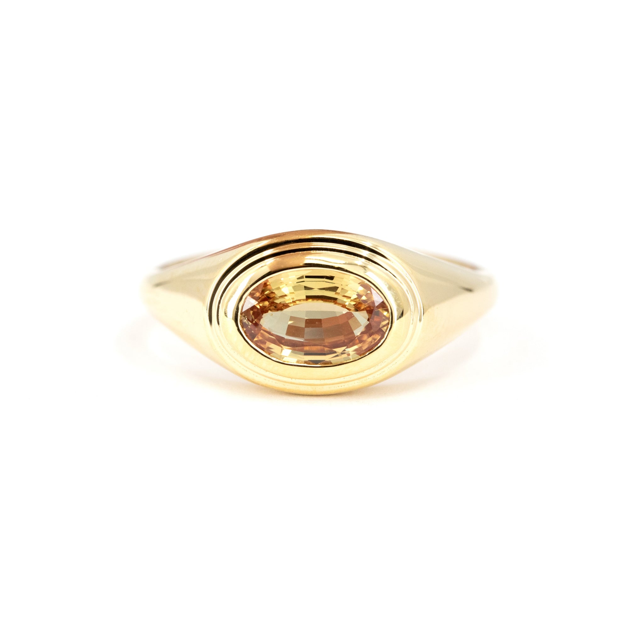 Close-up of a yellow gold ring with an oval champagne sapphire in a bezel setting, designed by Bena Jewelry in Montreal, Canada.