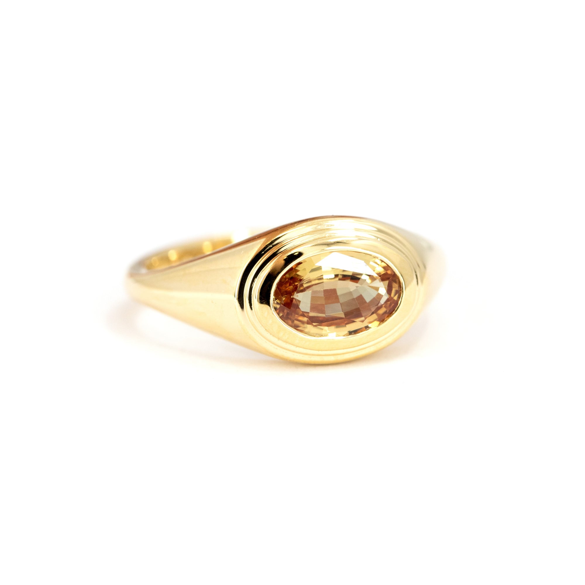 Contemporary yellow gold ring with smooth contours and a central oval champagne sapphire, crafted by Canadian designer Bena Jewelry.